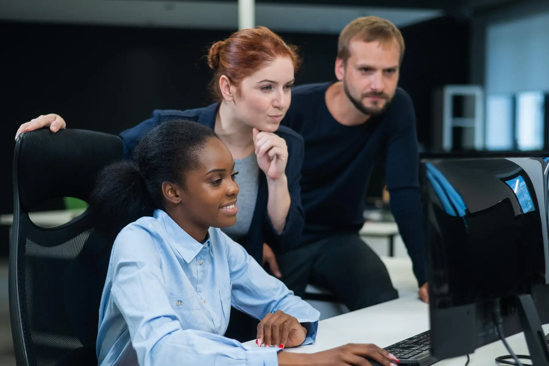 three people gathered behind a computer and staring at the display